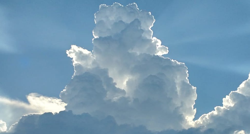 A cumulus cloud in a blue sky. The sun shines from behind the cloud, making it look grey.