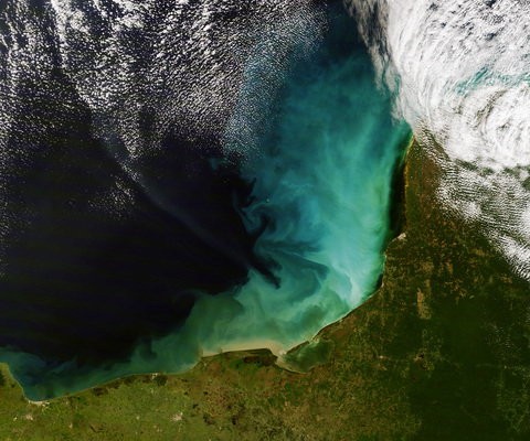 A satellite image of a white-ish green blob in a blue ocean near some green land.