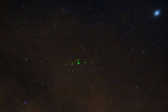 Green laser lights visible in a night sky